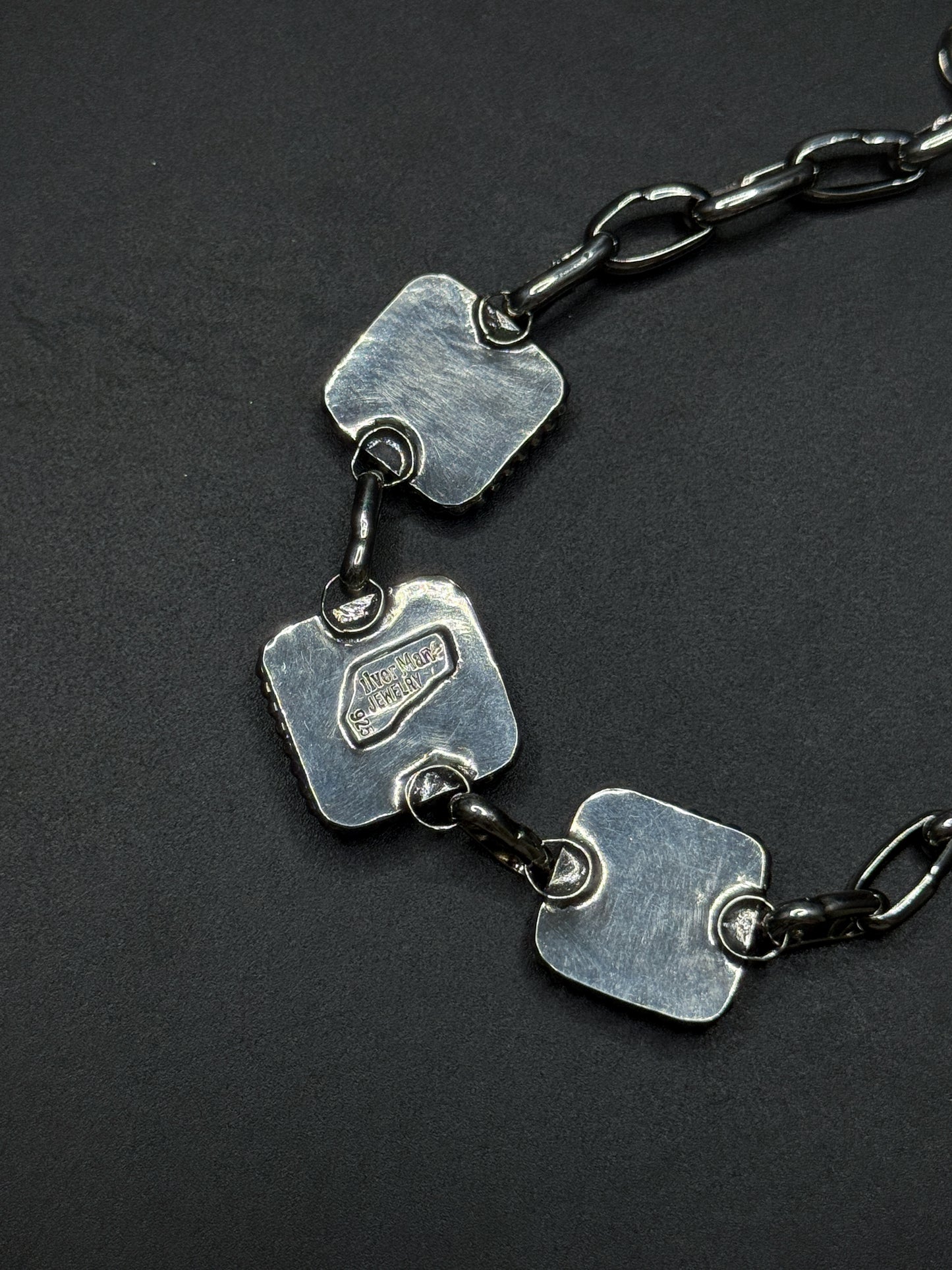 Silver necklace with square pendants on a dark background